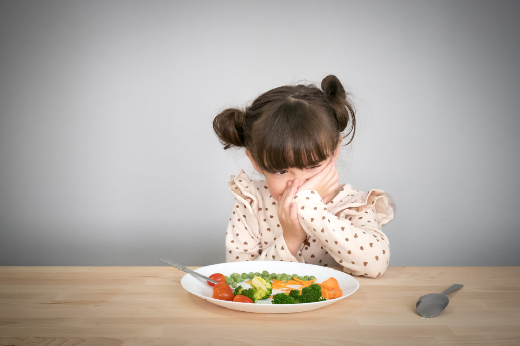 girl sitting in front of a plate of vegetables